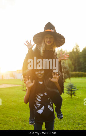 Portrait of two happy kids, boy and girl, having fun outdoors while posing in Halloween costumes lit by sunlight, copy space Stock Photo