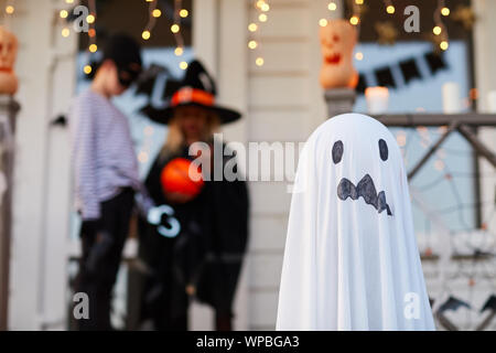 Background image of decorated house on Halloween, focus on ghost figure in foreground, copy space Stock Photo