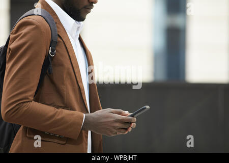 Mid section side view of African-American man holding smartphone and typing text messages in urban setting, copy space Stock Photo