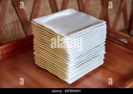 White square porcelain plates in large quantities on the counter of a store in artificial light. Contemporary square white plates stacked . Stock Photo