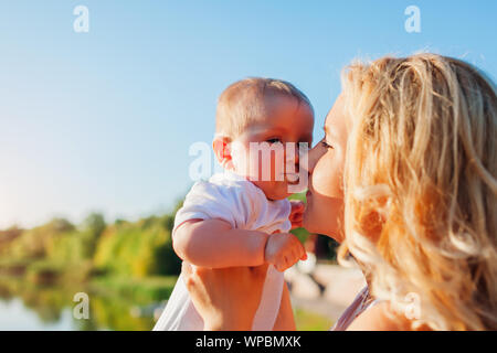 Young mother holding baby close to her face. Family walking in park at sunset Stock Photo