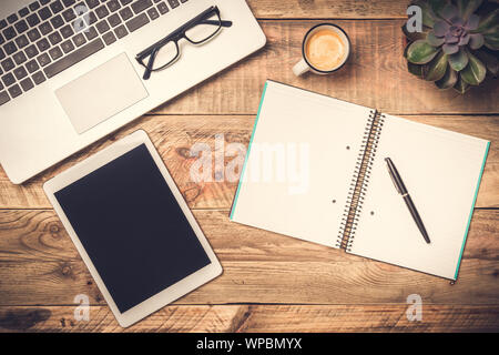 Laptop, computer tablet and open note book with white copy space on a rustic wooden table. Office work, workspace and desk top view concepts. Stock Photo