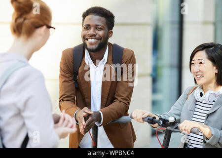 Group of contemporary young people chatting in city street, focus on African-American man smiling happily, copy space Stock Photo