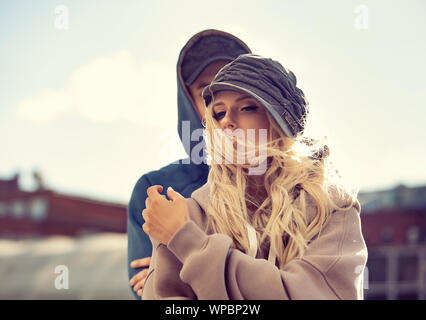 Stilish couple walking in modern hoodie sweatshirts and trendy hats  on autumn city old buildings background.  Closeup Stock Photo