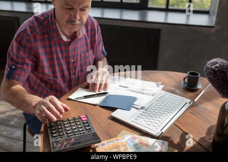 Senior hispanic man busy doing calculation, counting money and bills at home. He is looking through his taxes. Stock Photo