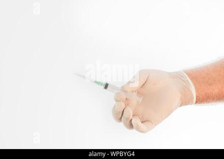 Close-up of the man's hand covered by a medical glove, holding a syringe on a white background. Space for writing. Stock Photo