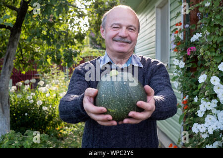 Senior hispanic man holding fresh seasonal green zucchini smiling being content with his autumn harvest. Stock Photo