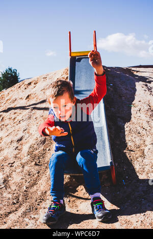 Child sliding down an old metal slide in a field. Stock Photo