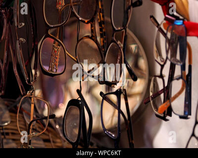 display of collection of eye-glass spectacles hanging vertically with different frames and distortions of various lenses in Cumbria, England, UK Stock Photo