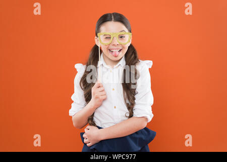 Child smart look through photo booth props eyeglasses. Small kid wearing eye glasses in smart style. School party concept. What does it mean being smart. Little smart schoolgirl on orange background. Stock Photo