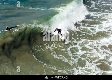 Huntington Beach, Calif. / USA - Sept 7, 2019: Two surfers in wetsuits. The young man is riding a wave while the woman is looking for the next wave. Stock Photo