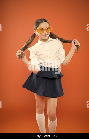 I am a girl and I am smart. Little smart schoolgirl on orange background. Adorable child with smart look through fancy glasses. Fashionable small kid wearing sunglasses in smart and chic style. Stock Photo