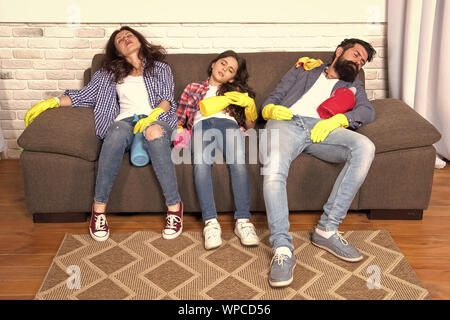 Exhausting cleaning day. Family mom dad and daughter with cleaning supplies sit on couch. Family care about cleanliness. Finish cleaning. Cleaning all day exhausting occupation. Tired parents and kid. Stock Photo