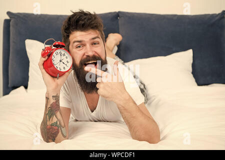 Time to wake up. Why you should wake up early every morning. Health benefits of rising early. Waking up early gives more time to prepare and be timely. Hipster bearded man lay in bed with alarm clock. Stock Photo