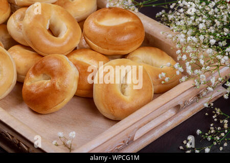 Close up of fresh mini bagels on wooden tray with flowers. Stock Photo