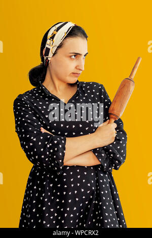 Angry wife waiting for her husband. Aggressive young middle-eastern woman holding dough rolling pin Stock Photo