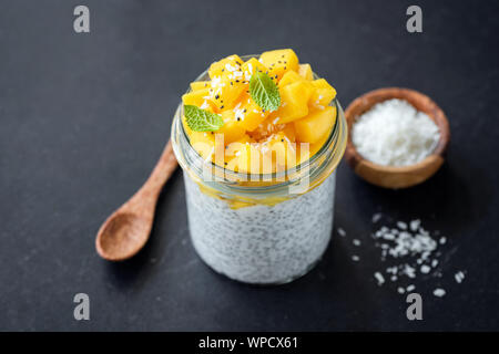 Healthy chia pudding with mango and coconut in glass jar on black background. Clean eating, dieting, healthy lifestyle concept Stock Photo