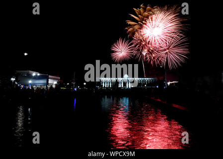 Colorful festive fireworks, salute over buildings in the city and its reflection in the fountain against the black sky Stock Photo