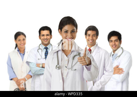 Confident female doctor showing thumbs up sign with team in the background Stock Photo