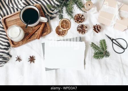 Christmas, winter composition. Blank greeting card mock-up scene. Cup of coffee, gift box, pine cones, fir branches, black scissors and candle on whit Stock Photo