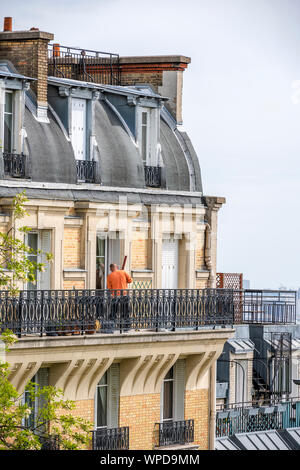 Man repairs his apartment in high-rise brick house with wooden shutters and residential attic and balconies outside the windows located on one of the Stock Photo