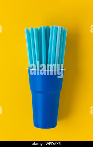 Dark blue plastic single use cup on yellow background. Many drinking straws inside the cup. Concept of recycling plastic and ecology. Top view. Stock Photo