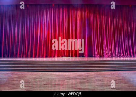 Red curtains and the stage parquet with stairs in theater with colorful lighting. Stock Photo
