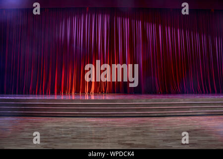 Red curtains and the stage parquet with stairs in theater with colorful lighting. Stock Photo