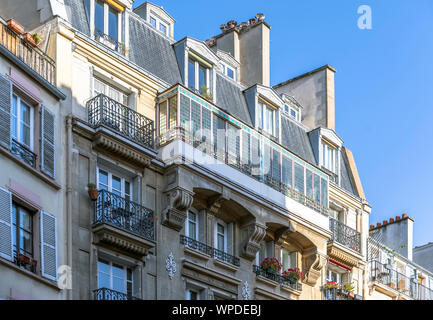 Hanging flower pots in the windows of the attic floor and on the balcony of multistory apartment building - a classic architectural design of old Pari Stock Photo