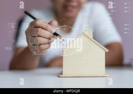 Happy Asian woman using pencil to draw a plan with wooden house piggy bank metaphor planning to saving money for buy the house select focus shallow de Stock Photo