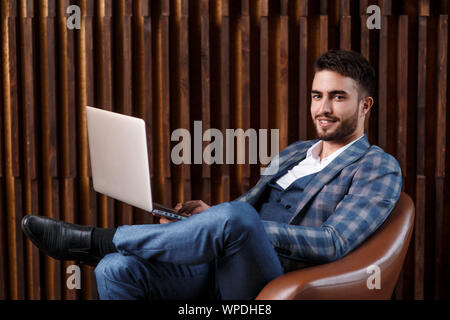 Young successful businessman is working behind a laptop while sitting in a loft office. bearded man working on a laptop. Stock Photo