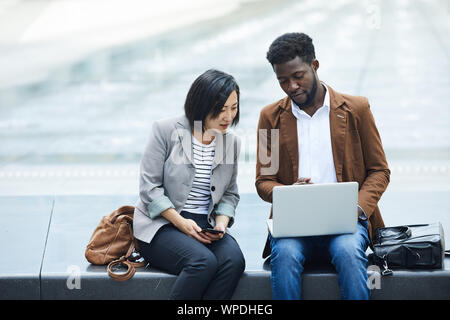 Portrait of two ethnic young people using laptop together outdoors while working on business project using wi-fi, copy space Stock Photo