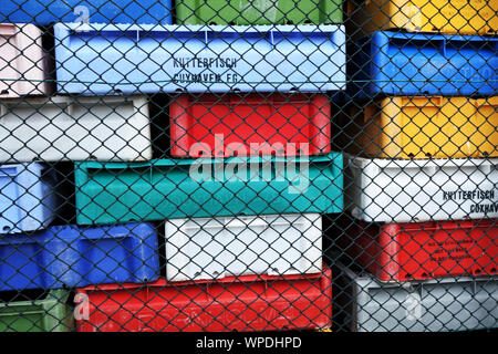 stacks of multicolored plastic fish crates used by fishermen at the Baltic Sea stacked behined wire mesh fence at fish factory. Stock Photo