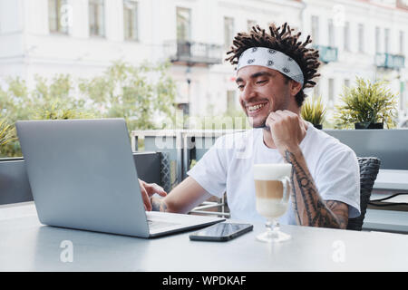 Excited hipster guy with dreadlocks hairstyle rejoice in winning an internet lottery made bets on website on laptop. Handsome bearded man celebrating Stock Photo