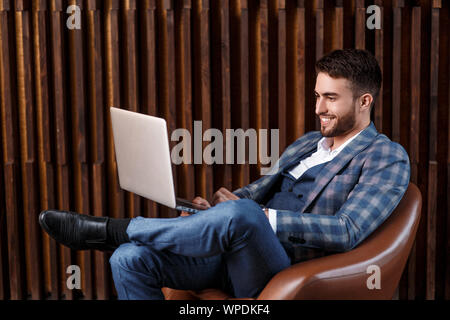 Young successful businessman is working behind a laptop while sitting in a loft office. bearded man working on a laptop. Stock Photo