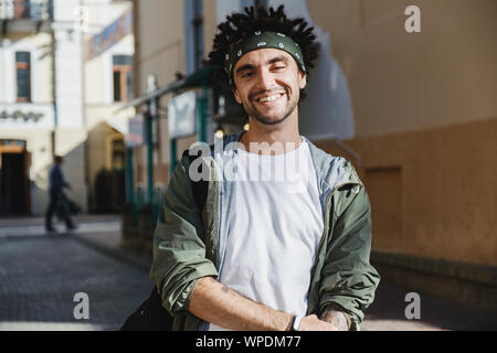 Smiling handsome man, happy hipster guy with dreadlocks hairstyle posing outdoor in the city street. Rastafarian lifestyle. Close up portrait of man d