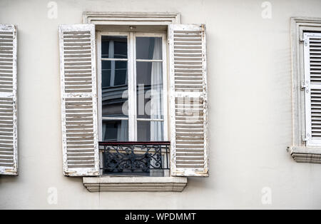 Window with the rickety shutters of an old stone multi-storey residential building with an impromptu balcony on the facade of a plastered multilevel h Stock Photo