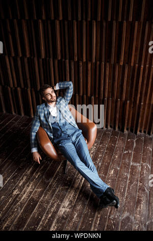 Young successful businessman in a blue suit in a cage is sitting in a leather chair. young man with a beard smiling Stock Photo