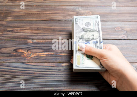 Female hand holding a bundle of one hundred dollar banknotes on wooden background. Salary and wage concept with copy space. Stock Photo