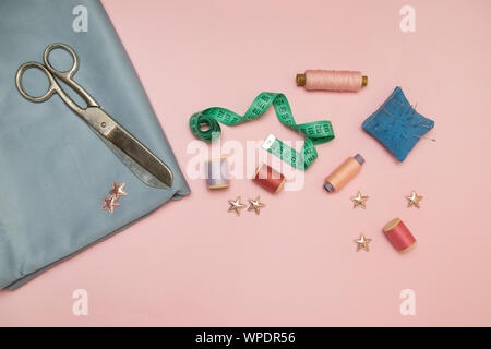 Needlework tools, blue knitted needlepoint for sewing, scissors and colored spools of thread on a pink background with copy space for text Stock Photo