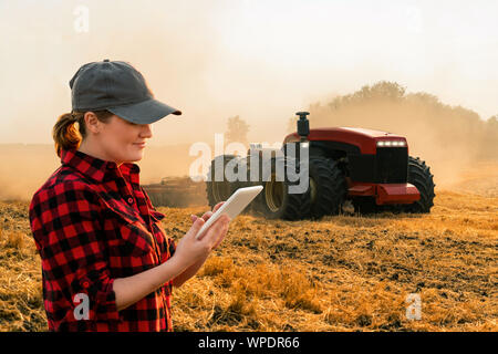 A woman farmer with digital tablet controls an autonomous tractor on a smart farm Stock Photo