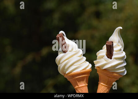 Two ice cream cones filled with soft whipped vanilla ice cream and chocolate flakes Stock Photo