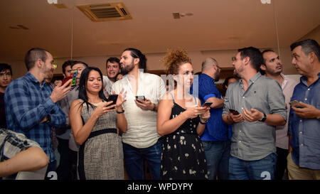 Coworkers gathered at a company party, using smartphones and socializing during a casual corporate event in an indoor setting. Stock Photo