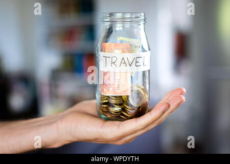 Man's hand holding a jar with euro coins and notes and a handwritten label saying travel. Stock Photo