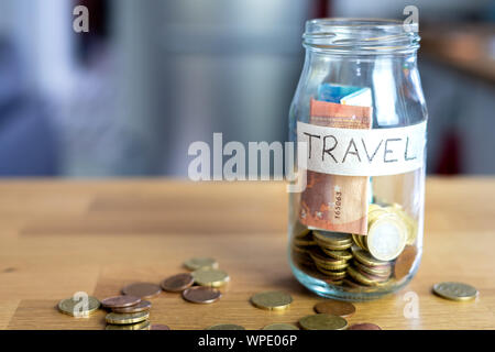 Transparent glass jar labeled travel with euro notes and euro coins inside. Euro coins outside on top of a wooden table. Stock Photo