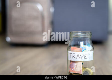 The glass jar on the floor labeled travel in focus and travel bag in the background out of focus. Wooden Floor. Stock Photo