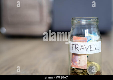 The glass jar on the floor labeled travel in focus and travel bag in the background out of focus. Wooden Floor. Stock Photo