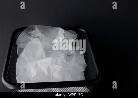 Plastic bag with handles, gloves in the bin on a black background . Used plastic bag for recycling. Concept - ecology, planet pollution with plastic Stock Photo