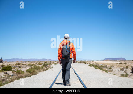 Young man traveler walking on the railway in the desert, steam locomotives cemetery at Uyuni, Bolivia, South America