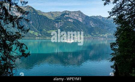 A tourist steamer boat travels across the crystal blue clear waters of the alpine Lake Brienz in Central Switzerland. Stock Photo